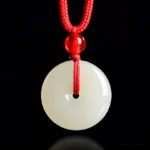 Natural jade peace buckle necklace with red rope pendant on black background - front flat lay view