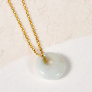 Jade donut pendant necklace flat lay on beige textured paper background showing pale green jade stone