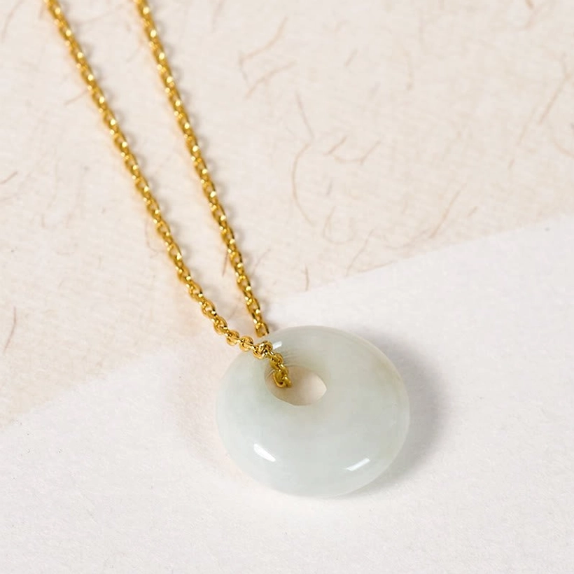 Jade donut pendant necklace flat lay on beige textured paper background showing pale green jade stone