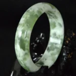 Natural jade prosperity bangle bracelet with green and white marbling, wide polished band design, top three-quarter view