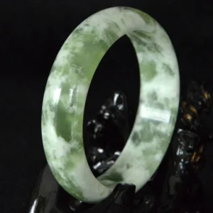 Natural jade prosperity bangle bracelet with green and white marbling, wide polished band design, top three-quarter view