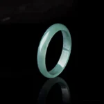 Natural jade prosperity ring handcrafted jadeite band side angle view with reflective backdrop