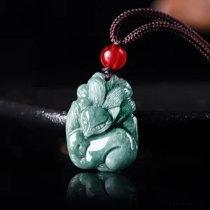 Natural green jade nine-tailed fox pendant necklace with brown cord and red bead accent, front close-up view on reflective surface