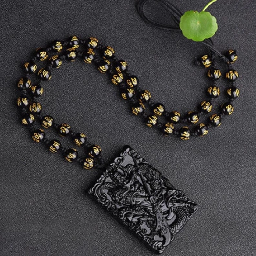 Black obsidian Lord Guan carved pendant with intricate Guangong and dragon pattern paired with black and gold mantra bead necklace, overhead flat lay composition