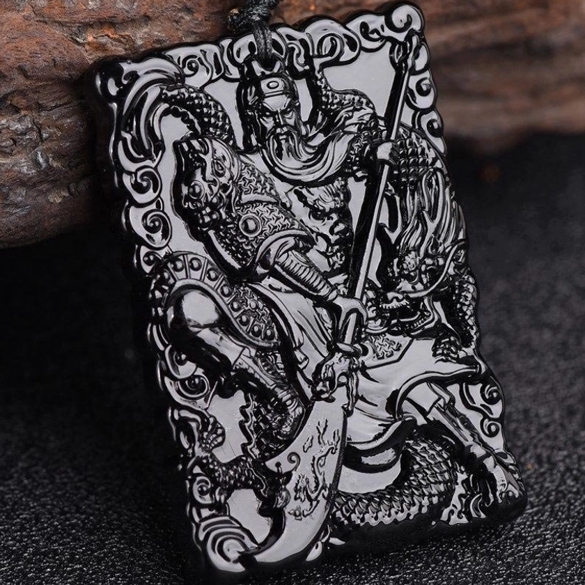 Black obsidian Lord Guan pendant side view showing intricately carved Guangong figure holding legendary broadsword with dragon pattern, polished glossy surface