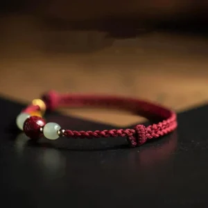 Prosperity jade bracelet three-quarter view showing braided red cord, jade beads, cinnabar bead, and gold spacer details