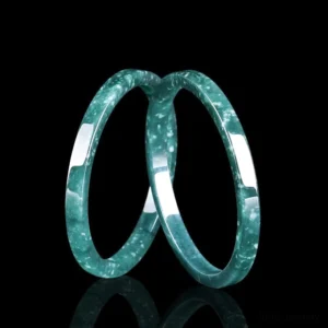 Two crossed natural jade thin bangles flat lay showing slim circular design and speckled green texture