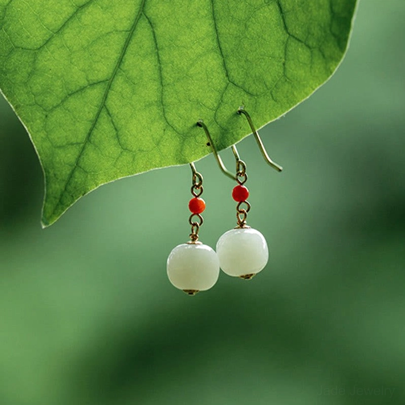 Pale off-white hetian jade drop earrings with red agate hanging against green leaf background