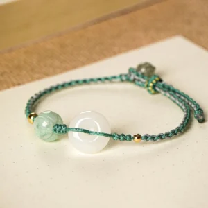Flat lay top view of adjustable white jade peace buckle bracelet with dark green cord and gold accents