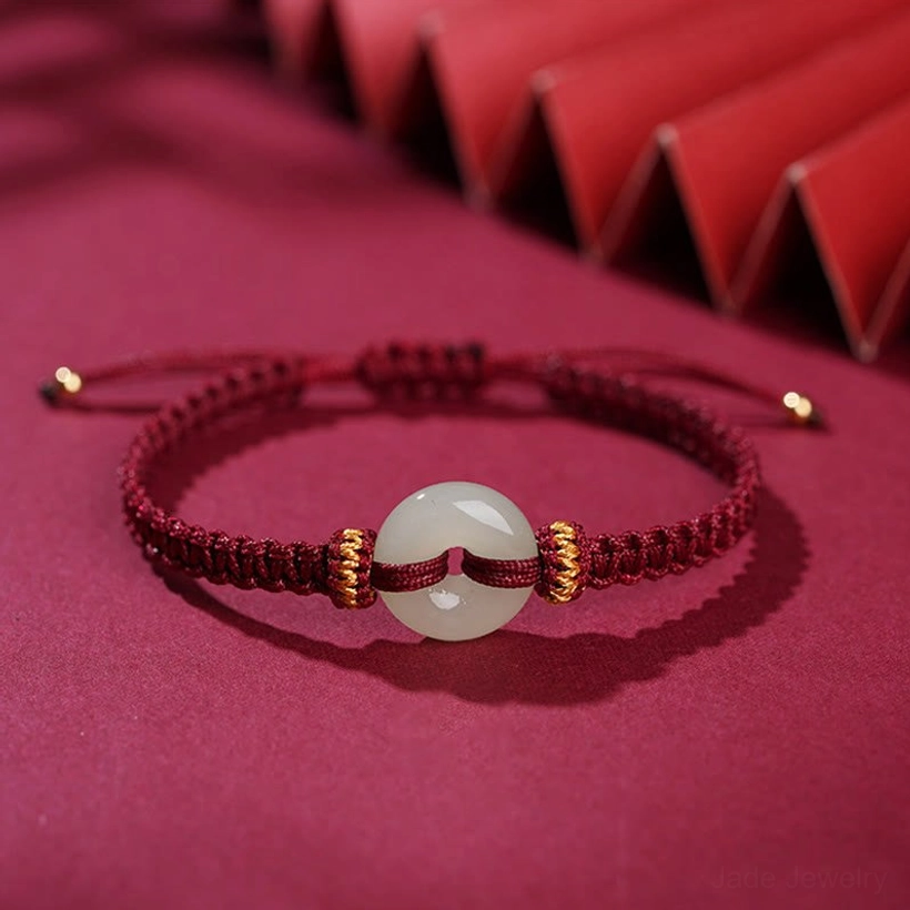 Detailed side flat lay of peace buckle jade bracelet showing braided wine-red rope, jade donut, and gold-tipped adjustable ends