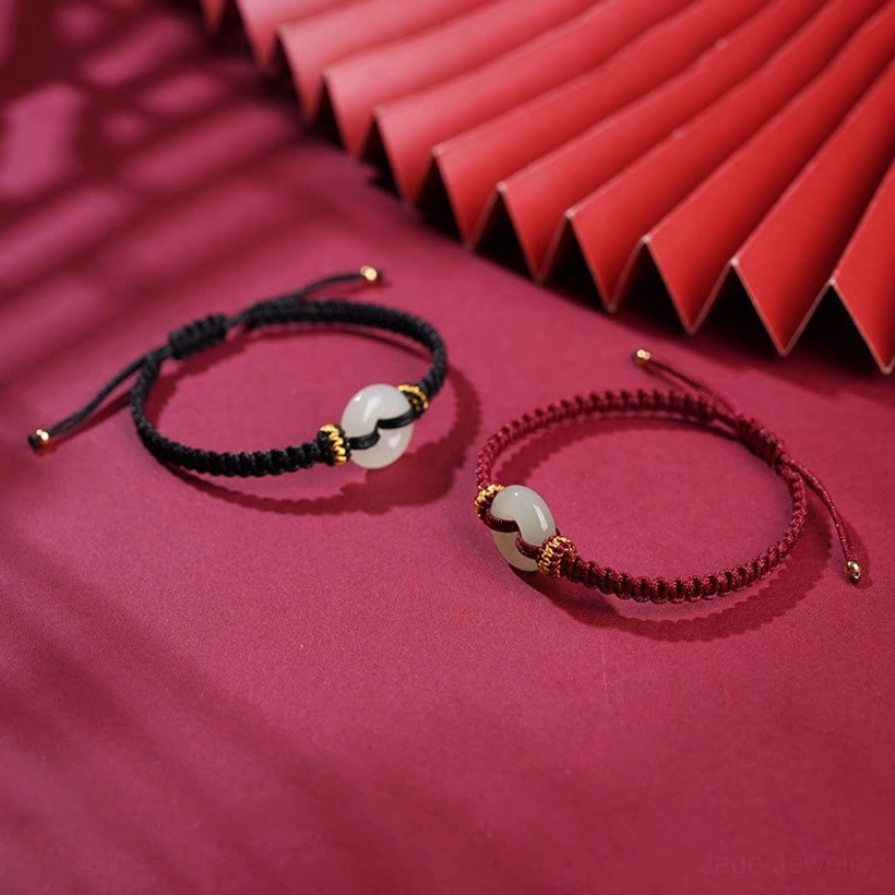 Two peace buckle jade bracelets side-by-side, one black cord and one wine-red cord, both with white jade pendants