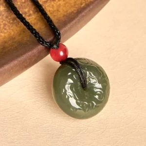 Ping an kou jade peace buckle necklace side view on brown wooden coaster, showcasing polished jade surface and embossed auspicious cloud patterns on black woven cord