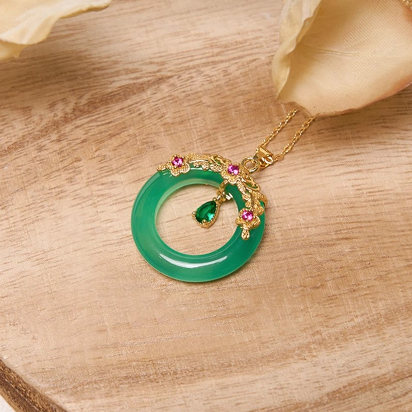 Green peace buckle pendant on wooden surface showing ornate gold frame and dangling teardrop charm