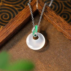 Natural chalcedony peace buckle pendant with green enamel bamboo leaf accent and silver chain, side angle view on vintage wooden tray