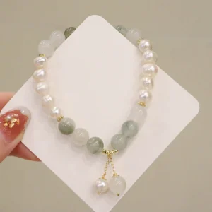 Close-up view of pearl jade healing bracelet held in hand on display card, featuring dual pearl drop charms and polished jade beads