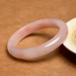 Pink Golden Silk Jade flat bangle bracelet overhead view on wooden surface