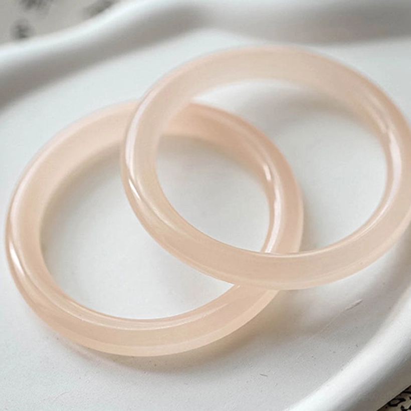 Pair of dusty rose pink jade bangles close-up flat lay, matching thin round translucent jade bands on ceramic tray
