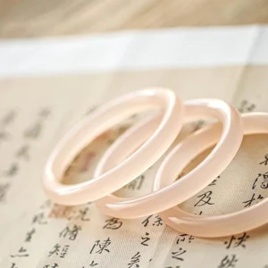 Set of authentic pink jade bangles flat lay, matching translucent rose jade pieces on vintage calligraphy fabric