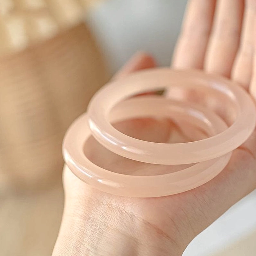 Stacked pink jade bangles held in palm close-up, three thin round polished rose jade pieces