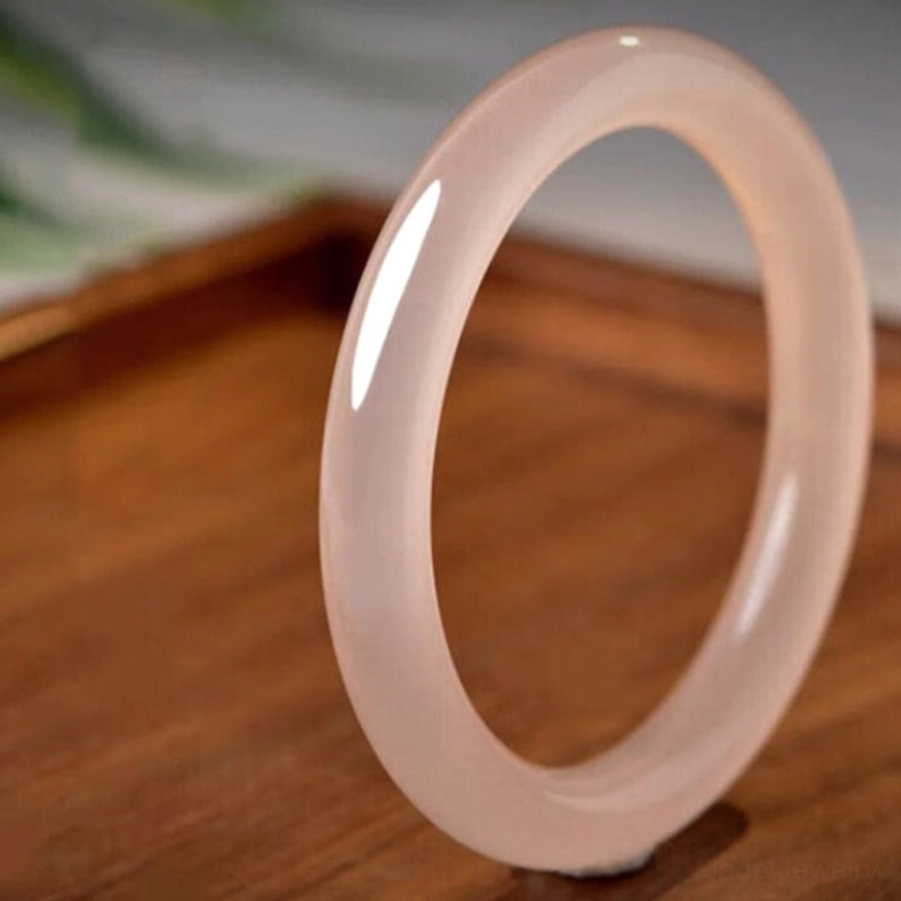 Single pink jade bangle studio shot, smooth round translucent rose jade on wooden table