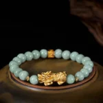 Golden Pixiu jade bracelet overhead flat lay with light green jade beads and gold charm on dark wooden tray