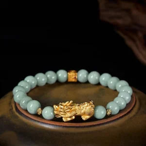 Golden Pixiu jade bracelet overhead flat lay with light green jade beads and gold charm on dark wooden tray
