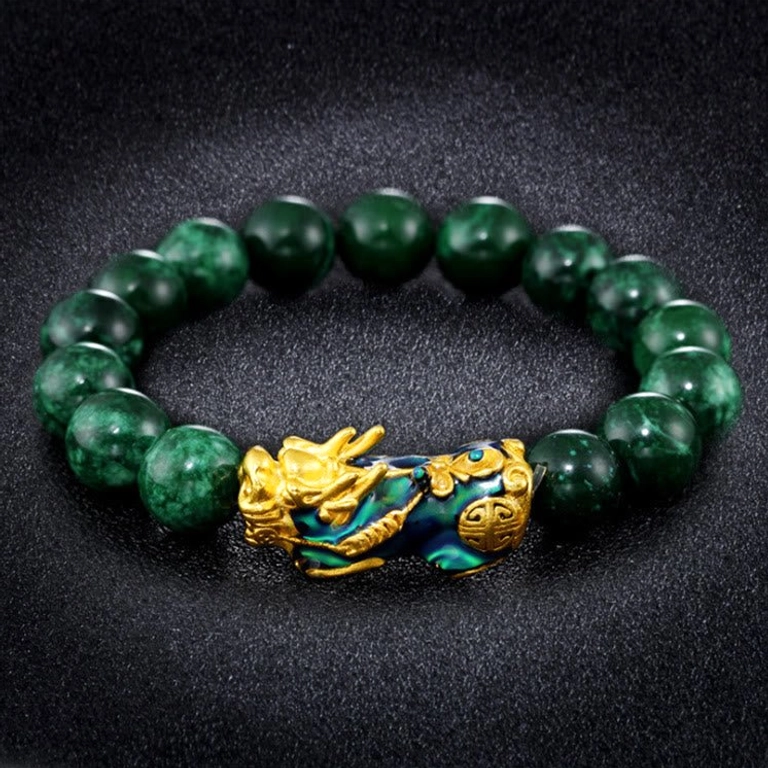 Overhead flat lay of Pixiu jade bracelet featuring deep green jade beads with enamel-accented gold Pixiu ornament on black matte background