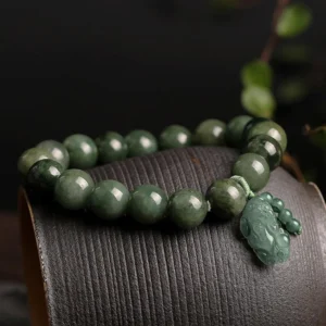 Jade Pi Xiu bracelet side view on leather texture with natural foliage, deep green carved charm detail