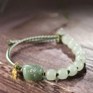 Natural Hetian jade Pixiu luck bracelet with gold charm on wooden surface - milky jade beads and dark green Pixiu
