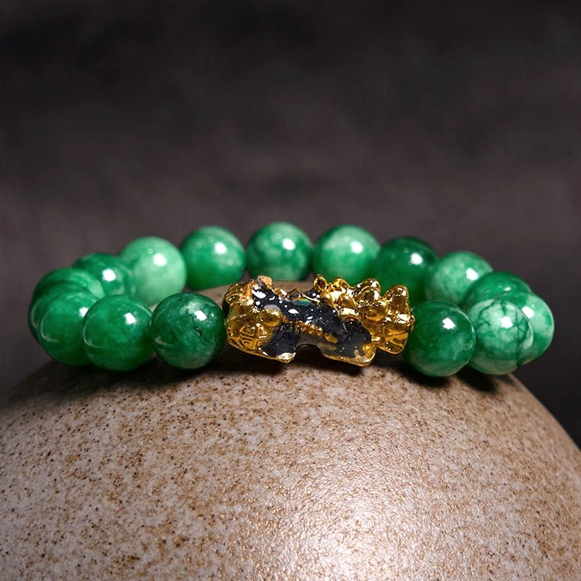 Close-up detail of Pi Xiu jade protection bracelet with vibrant round cyan jade beads and large gold-black enamel fortune beast charm on stone surface