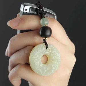 Hand holding carved pixiu jade peace buckle keychain attached to car remote showing embossed auspicious patterns