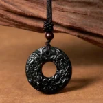 Black-green jade Pixiu peace buckle pendant with intricate carved Pixiu patterns, displayed on wooden surface with braided cord and wooden bead detail