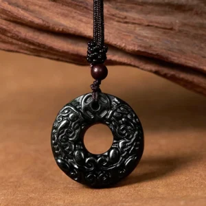 Black-green jade Pixiu peace buckle pendant with intricate carved Pixiu patterns, displayed on wooden surface with braided cord and wooden bead detail