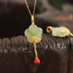 Vintage plum blossom jade pendant necklace with red agate accent on wooden background, showing delicate gold-toned metal work and light green carved jade