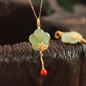 Vintage plum blossom jade pendant necklace with red agate accent on wooden background, showing delicate gold-toned metal work and light green carved jade