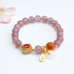 Purple chalcedony peace buckle bracelet with gold charm displayed on gray background with pink flowers