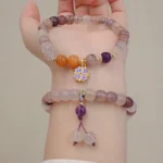 Purple golden silk jade bracelet with violet flower charm worn on two wrists, showing natural stone beads and protective energy