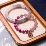 Purple jade bangle with strawberry quartz and tiger eye beaded bracelet set displayed on wooden tray with embroidered tablecloth