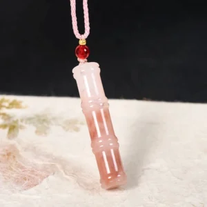 Flat lay front view of natural pink quartzite jade bamboo-carved pendant necklace on textured floral paper, showing organic mineral veining and artisan carving precision
