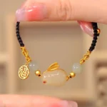 Year of the Rabbit jade bracelet with white jade beads and gold fu charm on black cord, overhead flat lay view