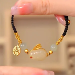 Year of the Rabbit jade bracelet with white jade beads and gold fu charm on black cord, overhead flat lay view