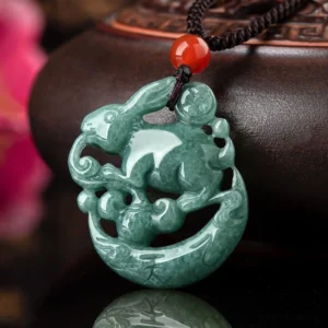 Year of the Rabbit jade crescent moon pendant necklace with red agate bead, deep green hollow carved jade, front view close-up on decorative display