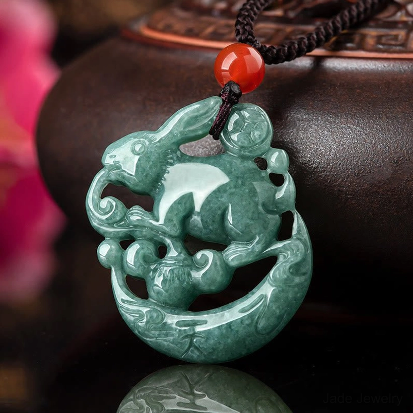Year of the Rabbit jade crescent moon pendant necklace with red agate bead, deep green hollow carved jade, front view close-up on decorative display