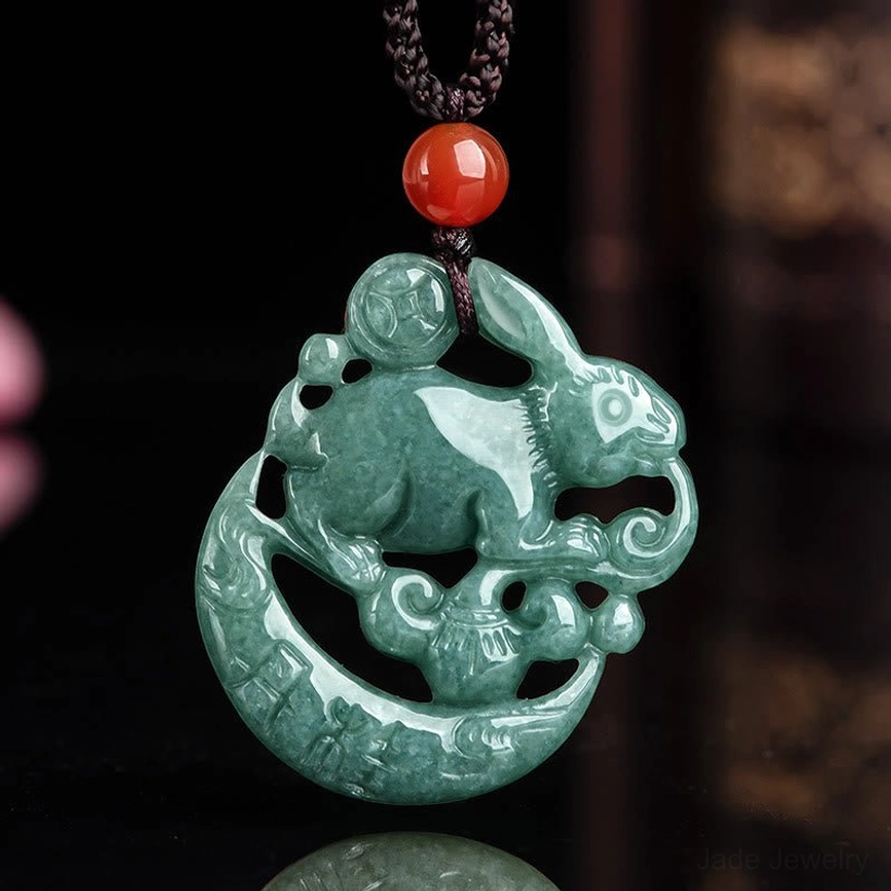 Reverse side of jade rabbit moon pendant showing intricate hollow carving details, red agate bead on black adjustable cord