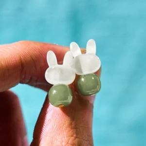 Hand-held rabbit jade earrings showing delicate design with copper posts and green stone pendants
