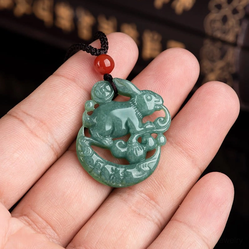 Hand-held jade rabbit crescent moon pendant necklace showing size comparison, red agate accent bead on black cord worn length