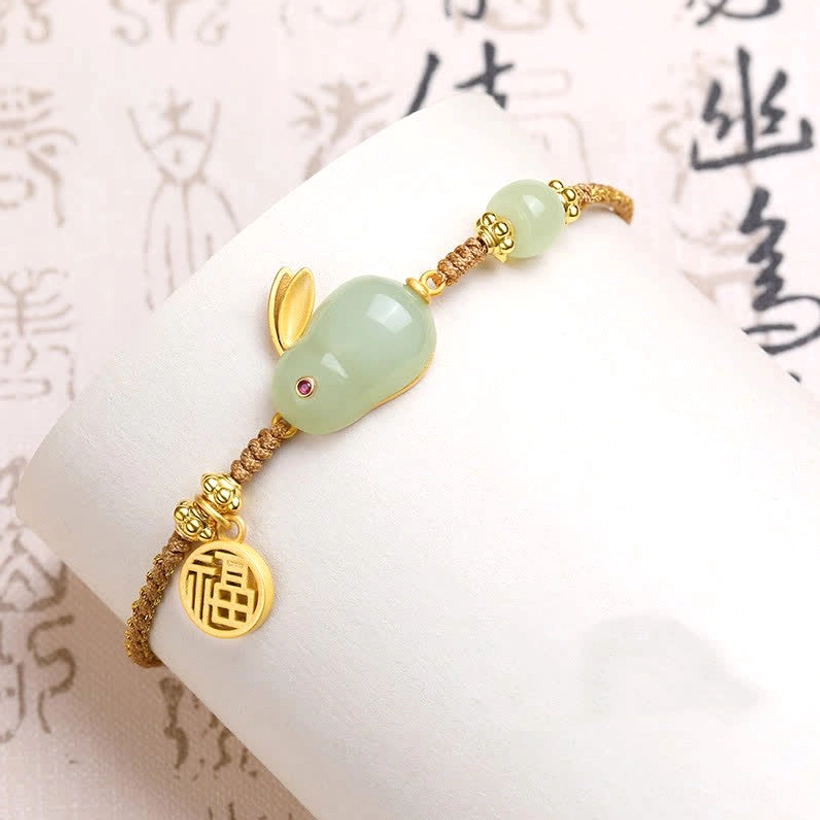 Hetian jade Rabbit bracelet with braided brown rope and golden accents on calligraphy backdrop