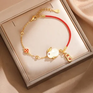 Year of the Rabbit jade bracelet with adjustable red string and gold chain accents, displayed in luxury jewelry gift box with fabric backdrop