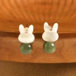 Lucky rabbit Hetian jade and Tridacna stone stud earrings with copper posts, front overhead view on wooden display