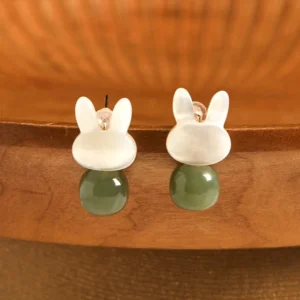 Lucky rabbit Hetian jade and Tridacna stone stud earrings with copper posts, front overhead view on wooden display